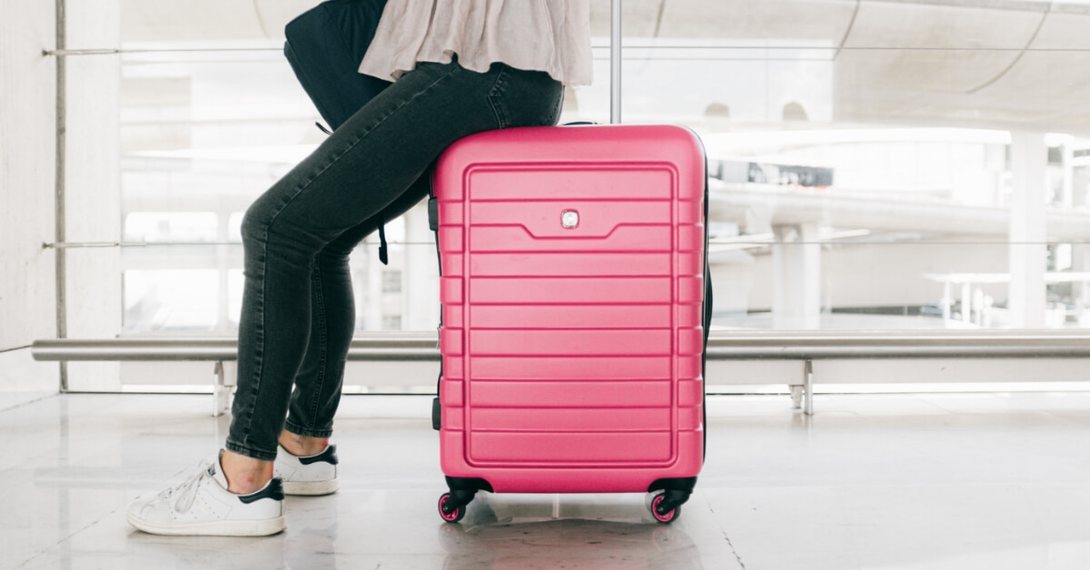 <img src="jak-spakować-walizkę"alt="kobieta siedząca na walizce i czekająca na samolot">
