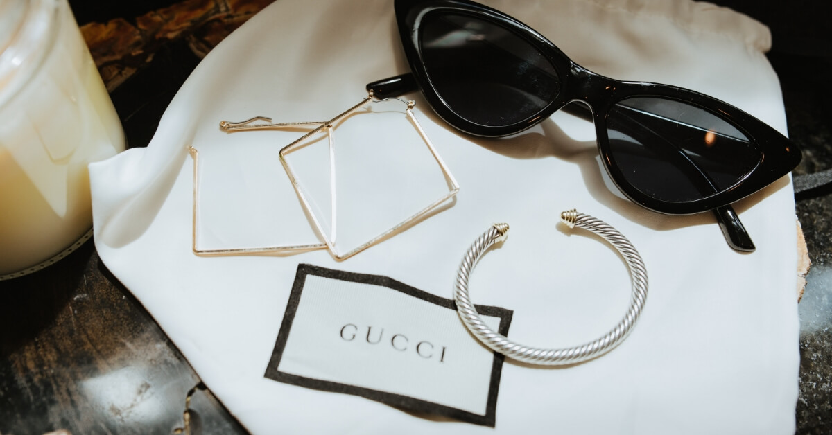 <img src="Historia-Gucci.jpg"alt="Okulary przeciwsłoneczne i dwa komplety kolczyków z wizytówką Gucci">