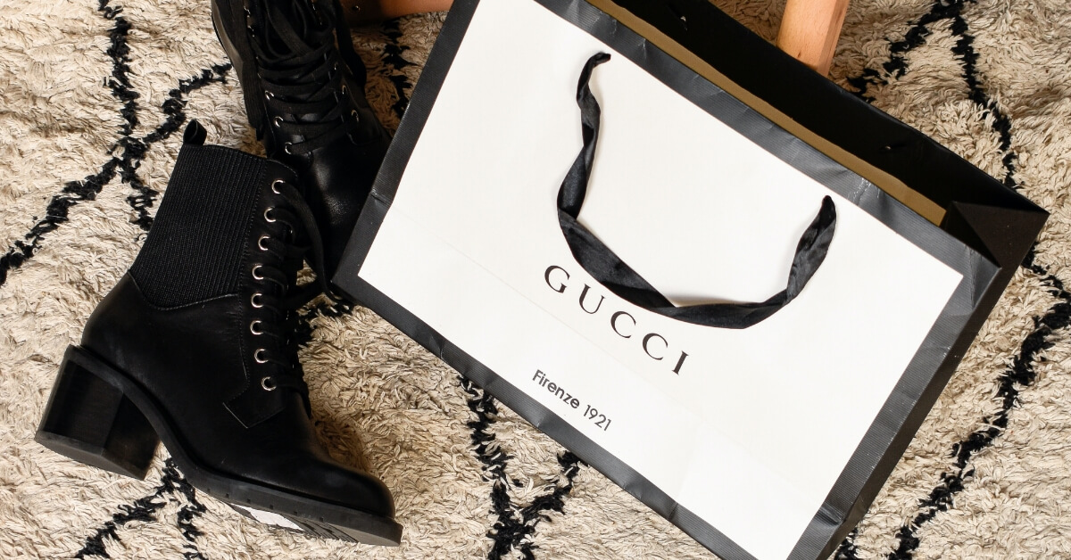 <img src="Historia-Gucci.jpg"alt="Czarne botki i torebka na zakupy ze sklepu Gucci">