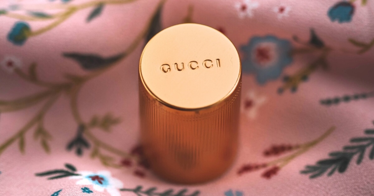 <img src="Gucci.jpg"alt="Sygnowane akcesorium logo Gucci położone na kwiatowej apaszce">